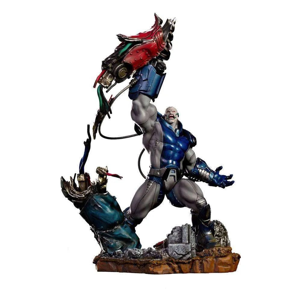 Iron Studios 1/10 Apocalypse Deluxe statue in blue and grey armor, lifting a mechanical arm on a rocky debris base.