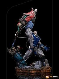 Iron Studios 1/10 Apocalypse Deluxe statue in blue and grey armor, holding a mechanical weapon aloft on a rocky base.