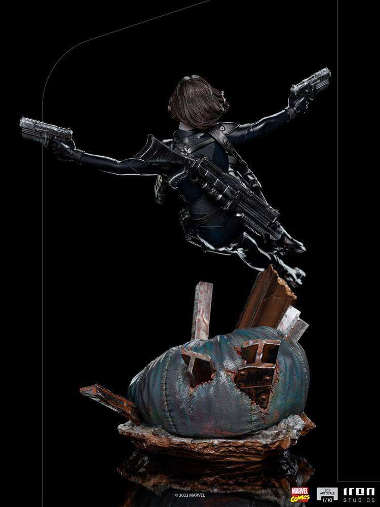 Rear view of Iron Studios 1/10 Domino statue in a black tactical suit, dual-wielding pistols atop a debris-filled base.
